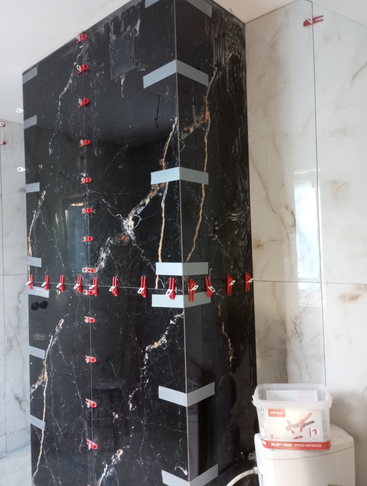 Czarne płytki imitujące marmur, ułożone w rogu łazienki w Katowicach, z użyciem klipsów poziomujących. Widoczny pojemnik z systemem poziomowania płytek.