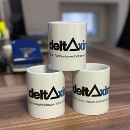Trzy białe kubki z logo biura rachunkowego Deltaxing Sp. z o.o. ustawione jeden na drugim na drewnianym biurku. W tle biurowe akcesoria.
