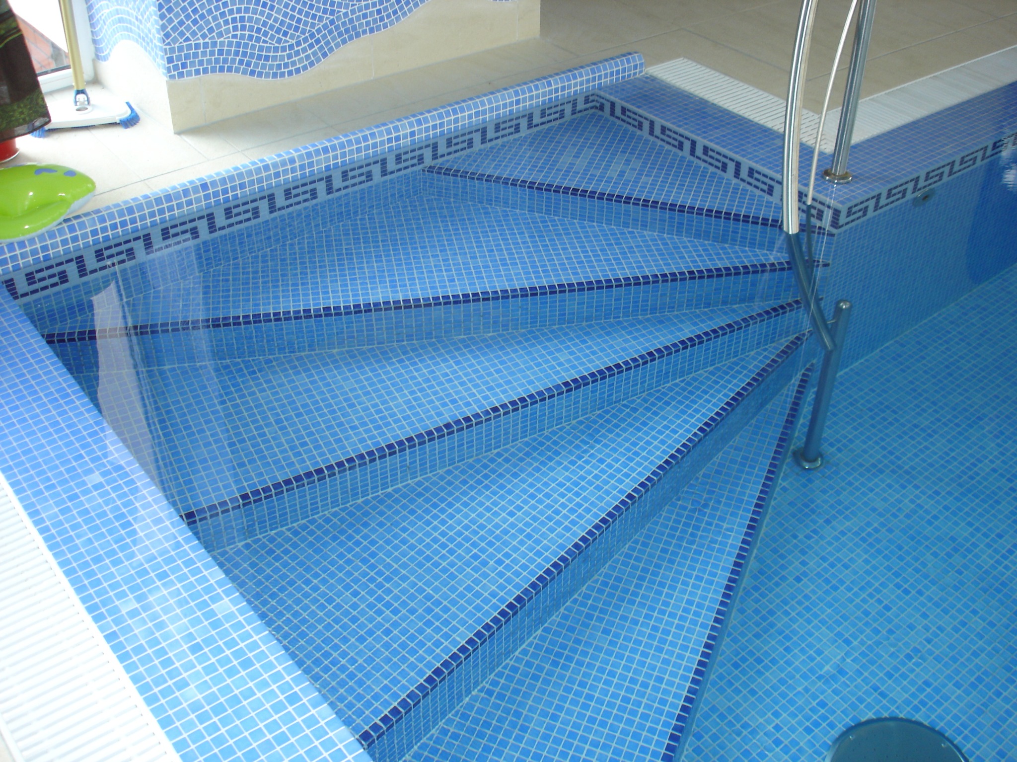 Błękitne mozaiki wykończonych schodów basenowych z metalową poręczą. Geometryczny wzór na krawędziach. Widok z góry na czysty, gotowy basen.