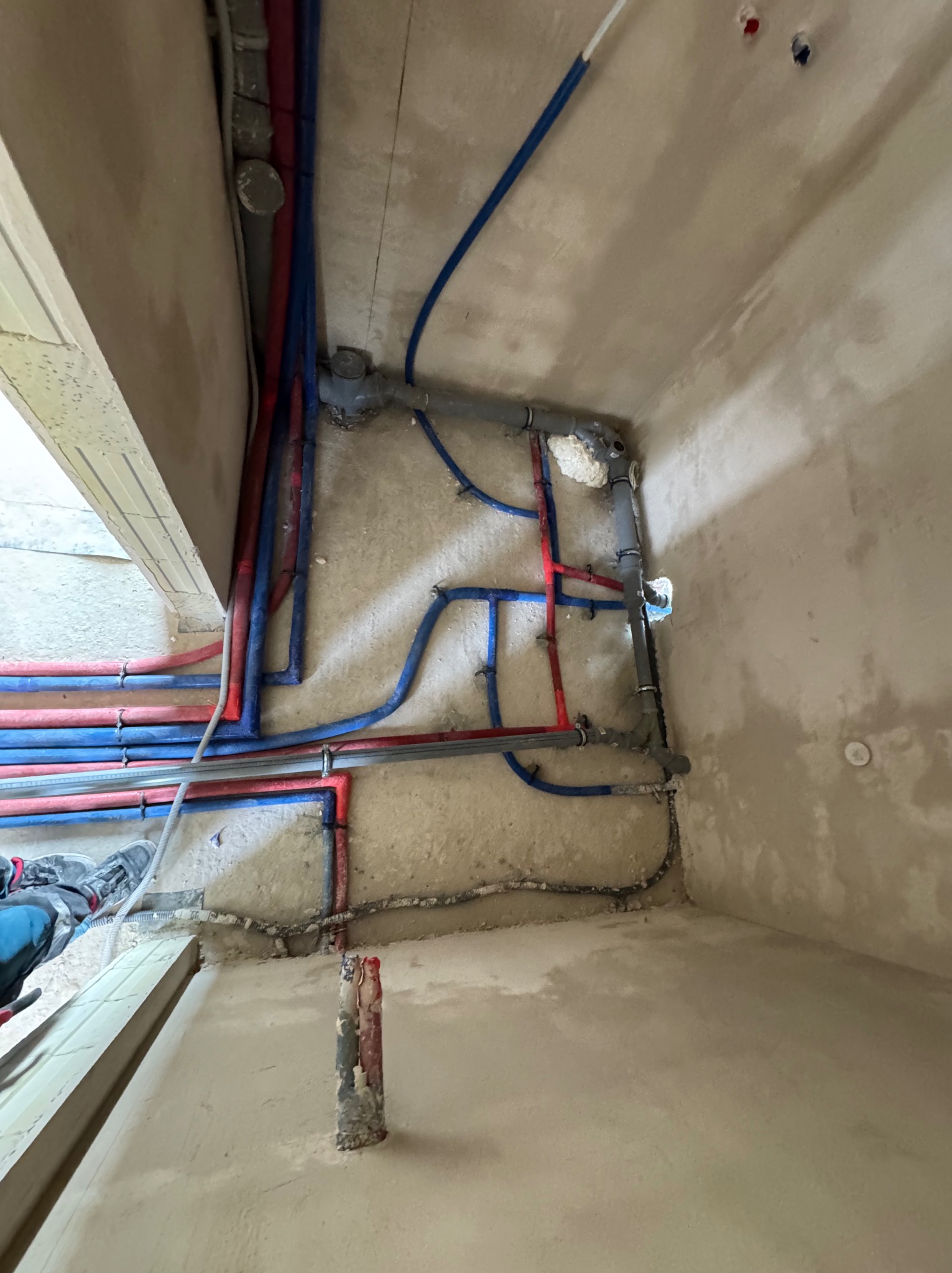 Rozbudowana instalacja wodna i grzewcza z rur PEX w kolorach niebieskim i czerwonym, zamocowana do surowej ściany w trakcie prac wykończeniowych.