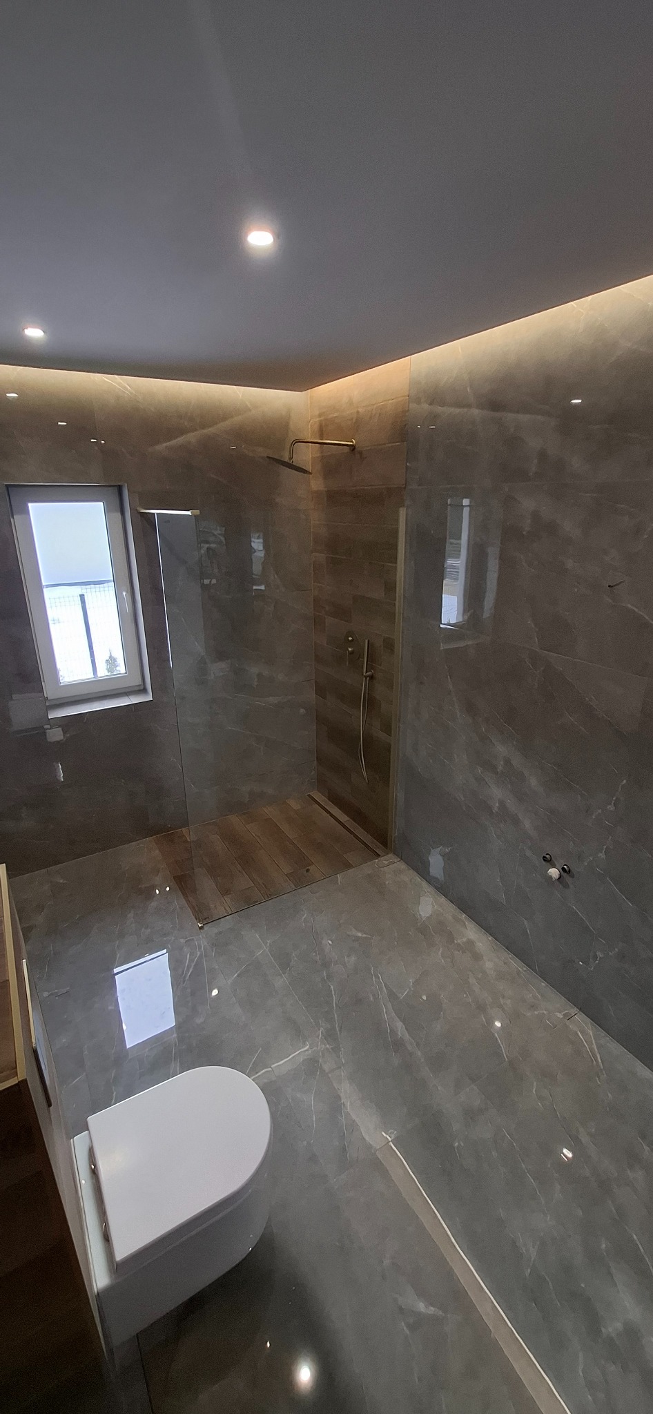 Elegancka łazienka z szarymi płytkami imitującymi marmur, kabiną prysznicową typu walk-in z drewnianym brodzikiem i podświetleniem LED na suficie.