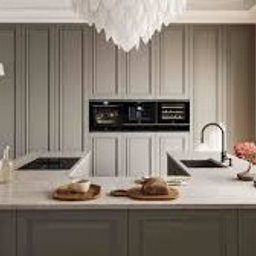 H.P. Agencja Nieruchomości - Elegancka, szara kuchnia z wyspą i wbudowanym sprzętem AGD. Na blacie dekoracje: bonsai, pieczywo, naczynia. W tle widok z okna na miasto. Nowoczesny design.