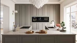 Elegancka, szara kuchnia z wyspą i wbudowanym sprzętem AGD. Na blacie dekoracje: bonsai, pieczywo, naczynia. W tle widok z okna na miasto. Nowoczesny design.