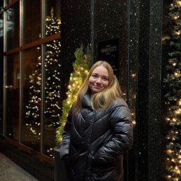 TwinView DroneFilm&Foto - Portret kobiety w czarnej kurtce na tle świątecznej dekoracji hotelu Grand City. W tle okno z choinką i światełka.