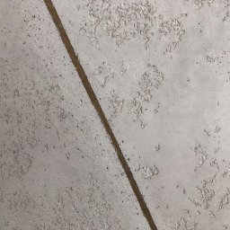 PI Development - Szpachlowana ściana z widoczną linią podziału, faktura z efektem dekoracyjnym. Jasnoszara kolorystyka, zbliżenie na fragment ściany z wyraźną strukturą.