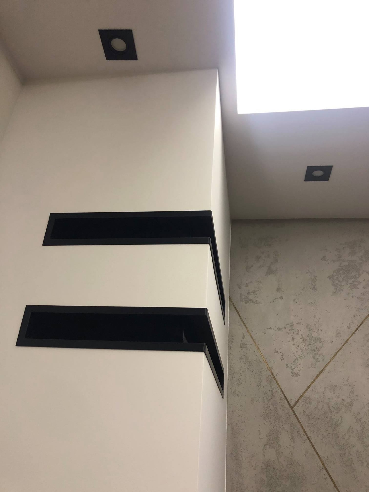 Nowoczesne wykończenie wnętrza: biała ściana z wnękami w czarnych obramowaniach, oświetlenie punktowe i dekoracyjna ściana z geometrycznym wzorem.