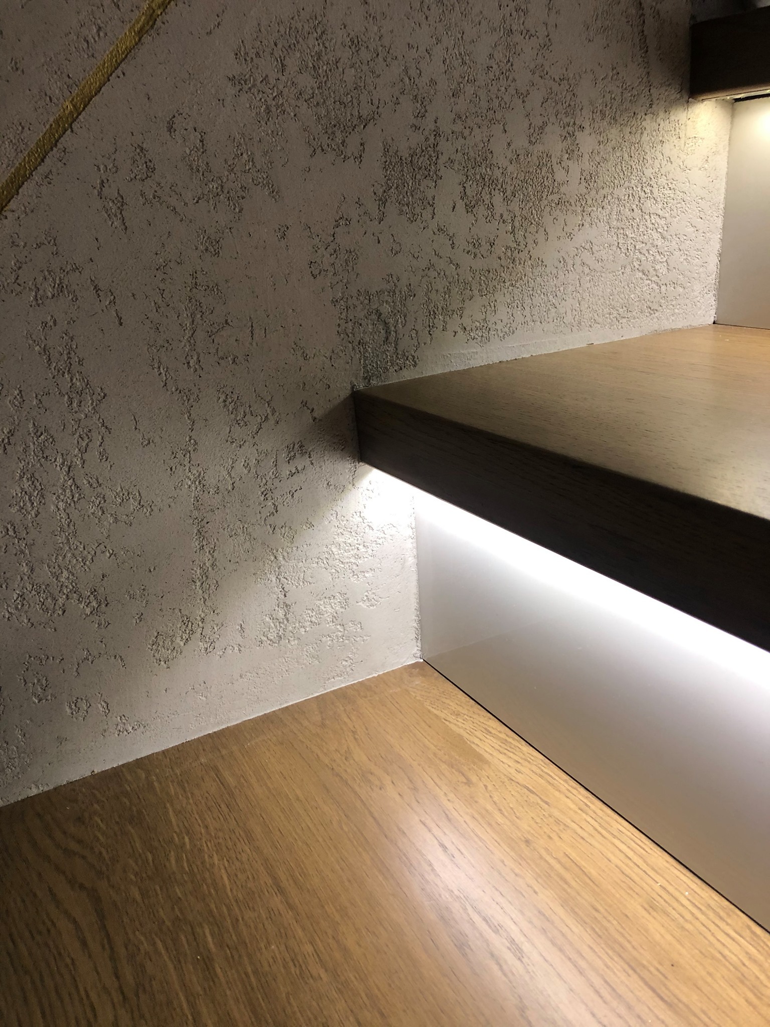 Ściana z dekoracyjną fakturą i drewniane schody z podświetleniem LED. Nowoczesne wykończenie wnętrza, ciepłe oświetlenie.