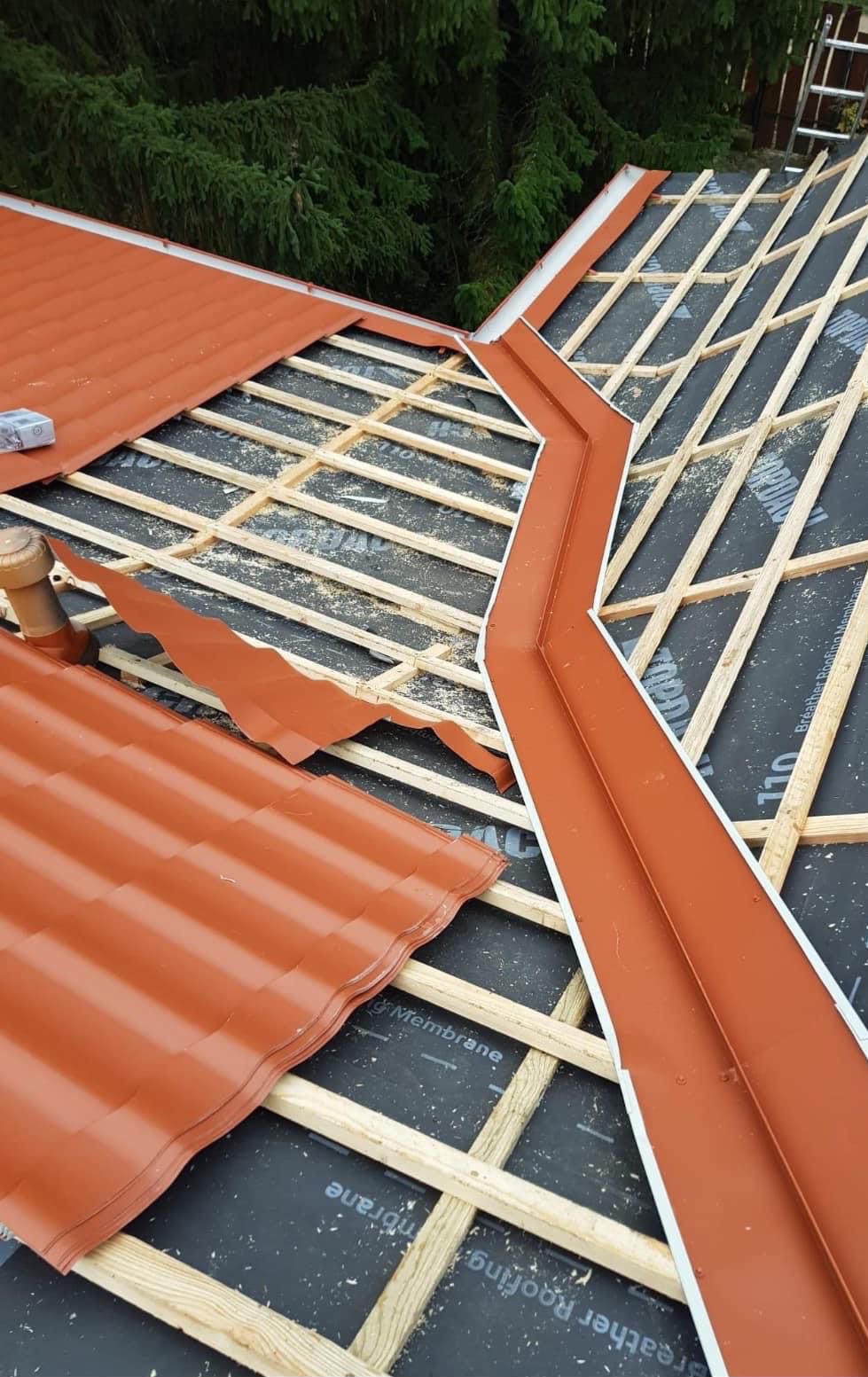 Częściowy widok na konstrukcję dachu z łatami, membraną i fragmentami czerwonej blachy trapezowej. Widoczne obróbki blacharskie i elementy wentylacji.