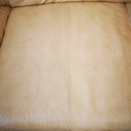 USŁUGI DŹWIGOWE ROBERT CIEŚLA - Jasnobeżowa, skórzana kanapa z widocznymi przeszyciami i delikatnymi zmarszczeniami na powierzchni siedziska. Widok z góry, ukazujący fakturę materiału.