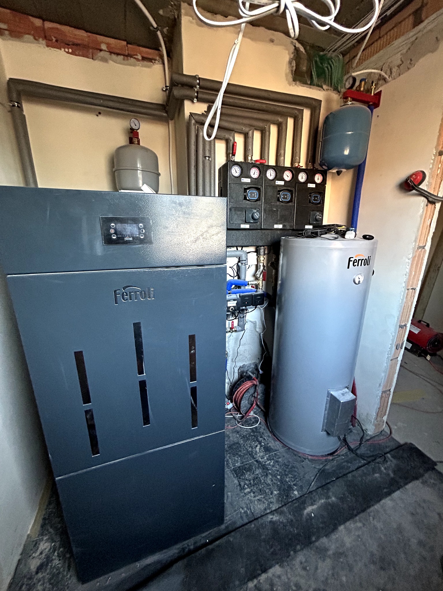 Nowoczesny piec gazowy Ferroli z zasobnikiem w kotłowni, widoczne rury instalacji CO i elementy sterujące. Ściany w trakcie wykończenia.