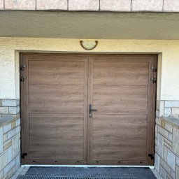 Andrzej Frąś montażownia - Dwuskrzydłowa brama garażowa w odcieniach brązu z poziomymi panelami, zamontowana w jasnym budynku z elementami kamiennymi i balustradą na górze.