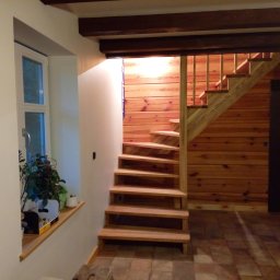 TOMASZEWSKI MEBLE PAWEŁ TOMASZEWSKI - Drewniane schody spiralne z jasnego drewna, prowadzące na górę, z drewnianą balustradą. Ściany wykończone boazerią. Obok okno z roślinami.