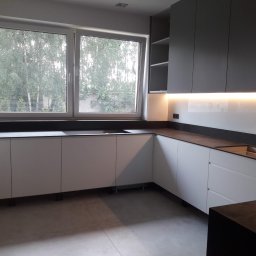 TOMASZEWSKI MEBLE PAWEŁ TOMASZEWSKI - Nowoczesna kuchnia z białymi szafkami dolnymi i szarymi górnymi, podświetleniem LED i widokiem na zieleń za oknem. Minimalistyczny design, ciemny blat.