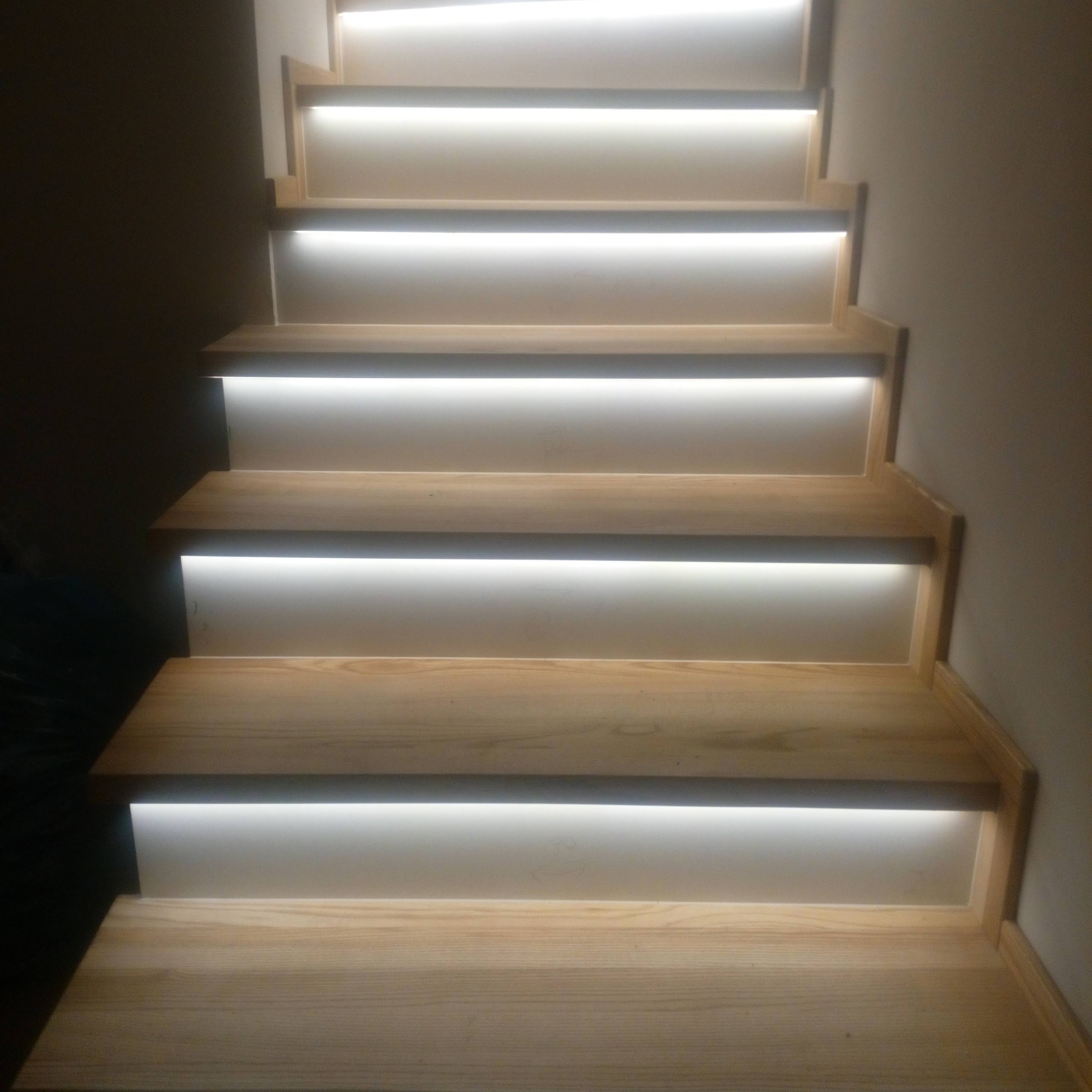Drewniane schody z podświetleniem LED w Prabutach. Widok z dołu, ukazujący jasne, naturalne drewno i nowoczesne oświetlenie, tworzące unikalny efekt wizualny.