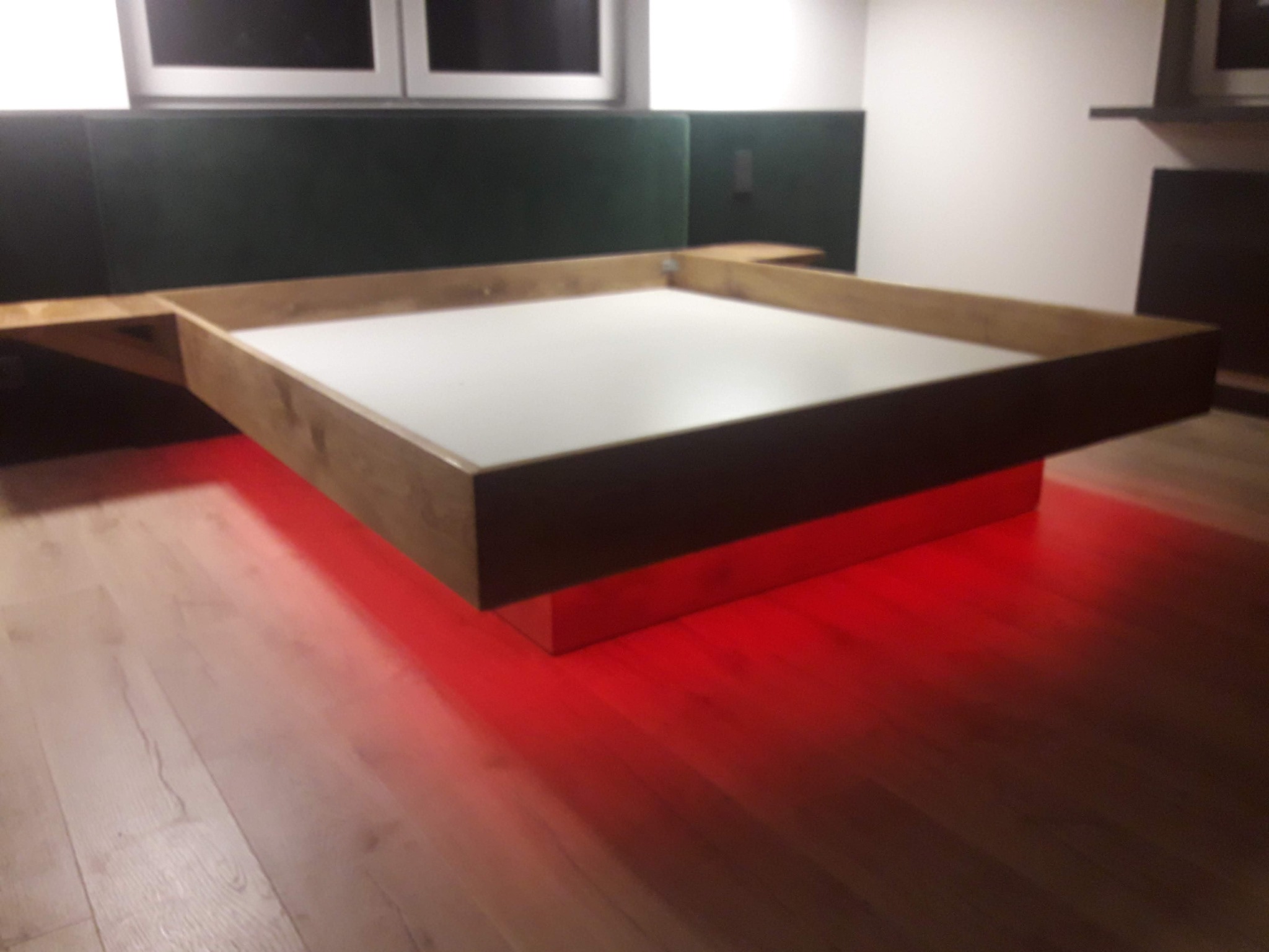 Nowoczesna antresola z podświetleniem LED w Prabutach. Drewniana konstrukcja z białym blatem, czerwone światło odbija się od podłogi. Nietypowe rozwiązanie aranżacyjne.