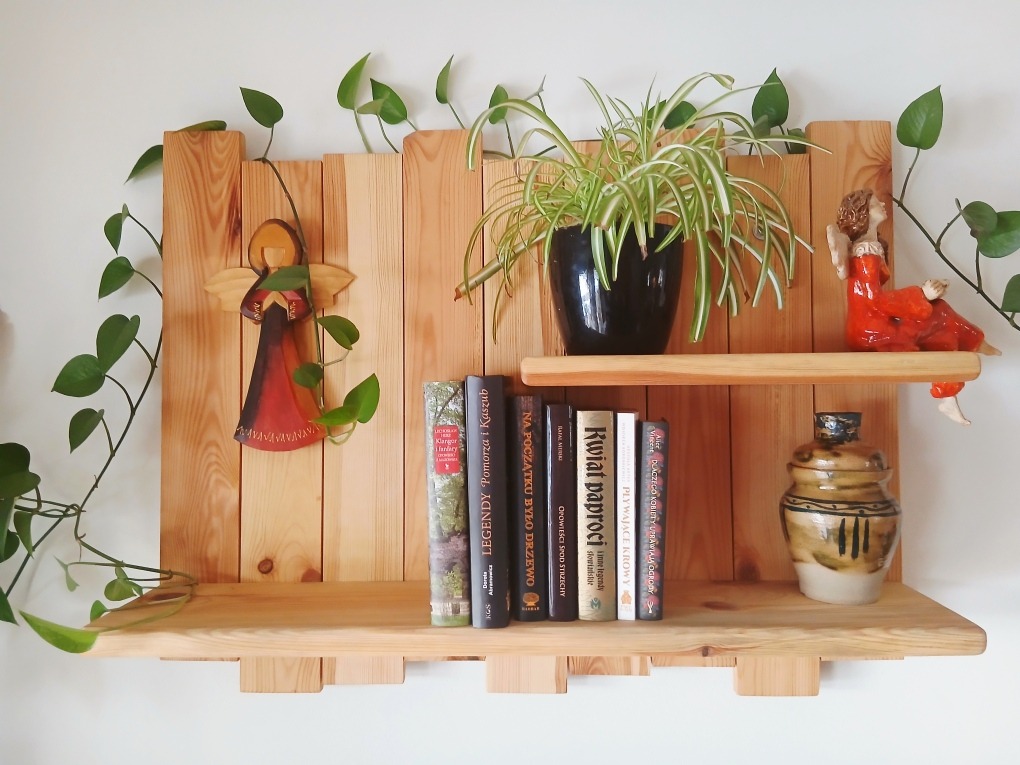 Drewniana półka z desek, zdobiona figurką anioła, roślinami doniczkowymi i książkami. Naturalne drewno, jasne tło, ciepłe oświetlenie. Dekoracyjny element wystroju wnętrza.