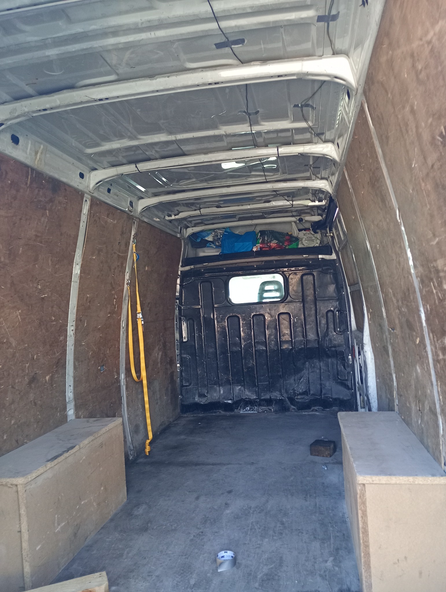 Wnętrze dostawczego busa z drewnianą zabudową ścian i podłogi, widoczne pasy mocujące i skrzynie. Pusta przestrzeń ładunkowa gotowa do transportu.