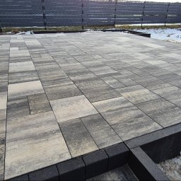 Umyję Umebluję Kamil Klonowski - Ułożona kostka brukowa w Nakle nad Notecią. Szaro-beżowa kostka tworzy wzór na tarasie. Widoczne czarne obrzeża i fragmenty śniegu.