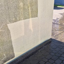 Umyję Umebluję Kamil Klonowski - Fragment elewacji budynku z widocznym efektem czyszczenia. Część ściany jest czysta, a część pokryta zabrudzeniami. Na dole leży lanca do myjki ciśnieniowej.
