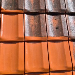 Częściowo wyczyszczona, pomarańczowa dachówka ceramiczna. Górna część dachu pokryta ciemnym nalotem, dolna - czysta, w intensywnym pomarańczowym kolorze. Widoczny efekt przed i po.