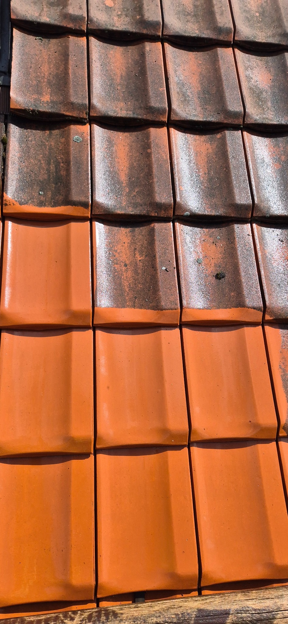 Częściowo wyczyszczona, pomarańczowa dachówka ceramiczna. Górna część dachu pokryta ciemnym nalotem, dolna - czysta, w intensywnym pomarańczowym kolorze. Widoczny efekt przed i po.