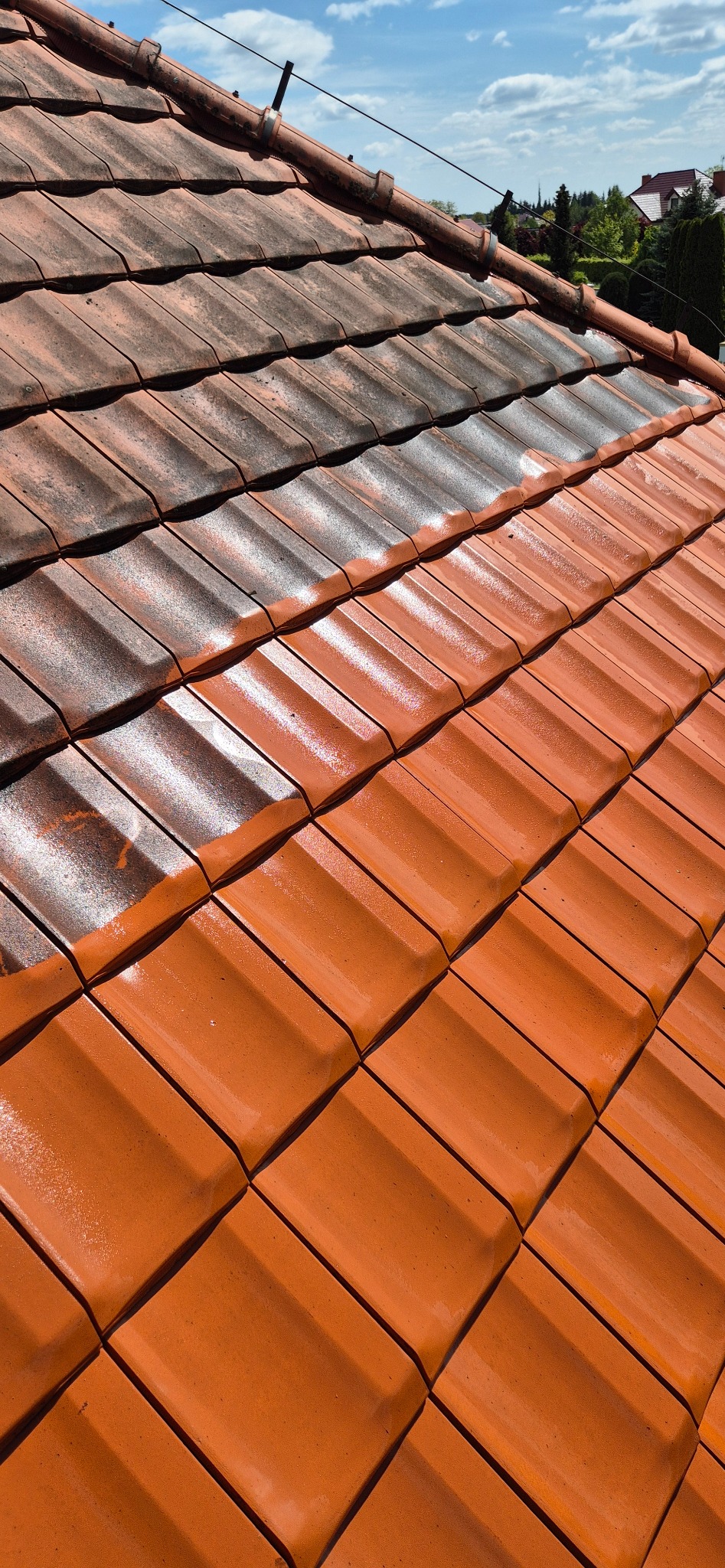 Częściowo wyczyszczony dach z czerwonej dachówki. Górna część dachu jest brudna, dolna czysta. Widoczna różnica w kolorze i czystości. Ujęcie z góry.