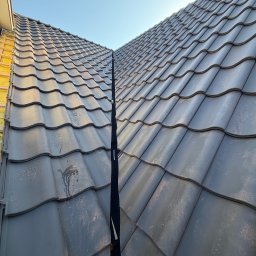 Stanidak - Nowy, ciemnoszary dach z dachówki ceramicznej, widok z góry, z wyraźnie zaznaczonym kalenicą i fragmentem ocieplonej ściany szczytowej budynku w tle.