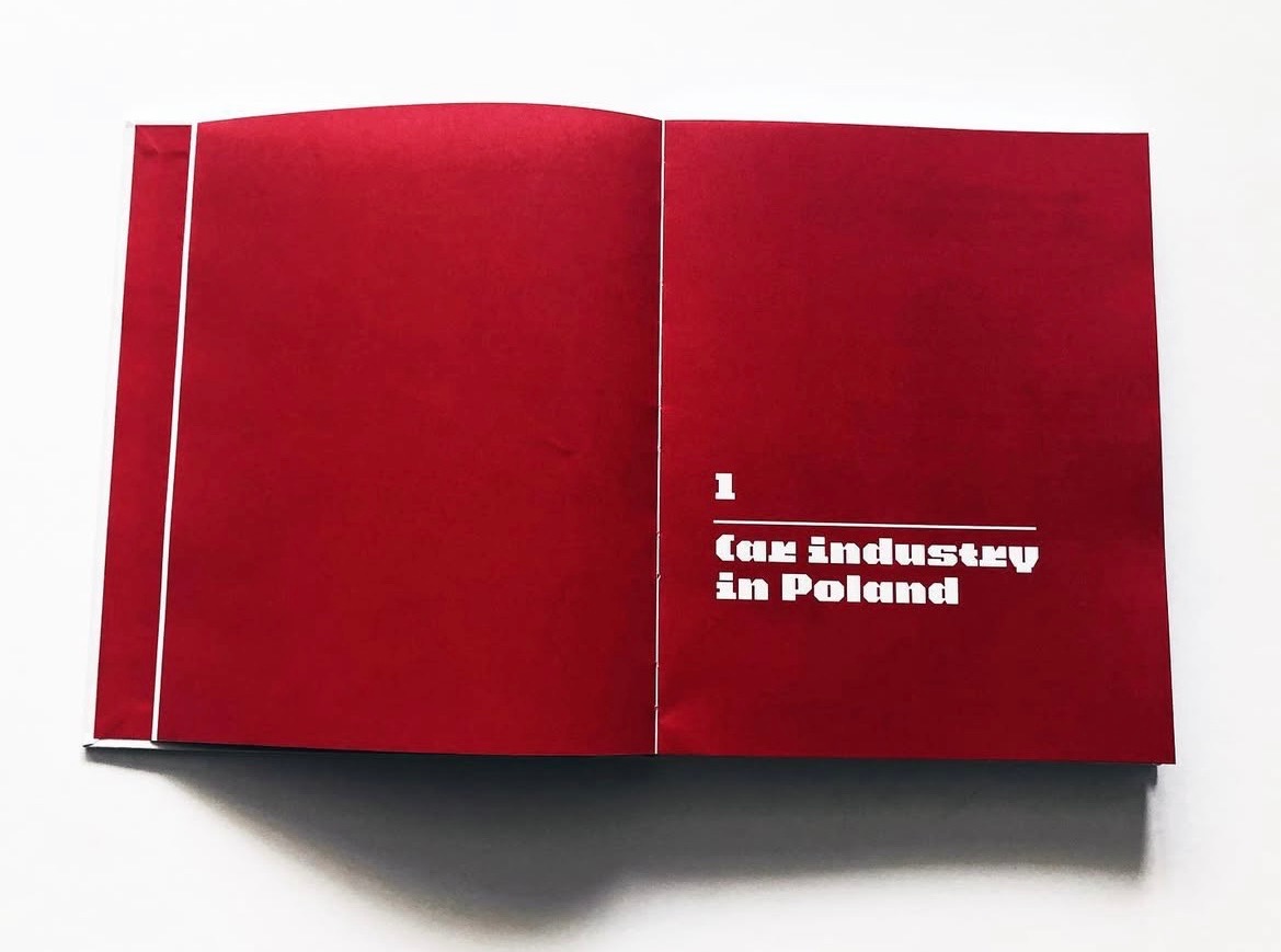 Otwarta, czerwona broszura z białym tekstem '1 Car industry in Poland'. Widoczny cień na białym tle. Minimalistyczny design, wyraźny kontrast kolorów.