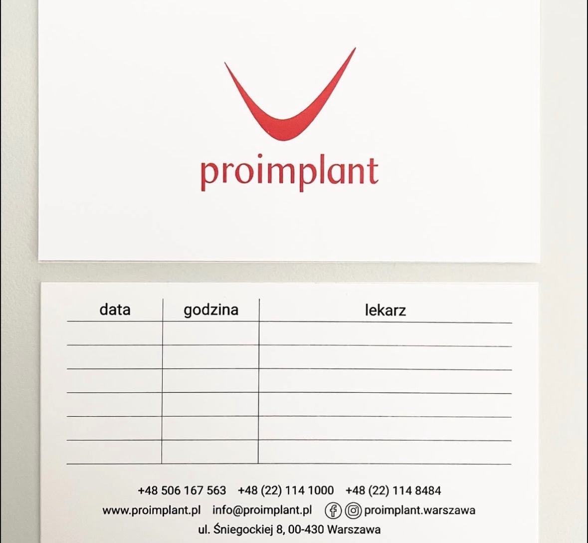 Wizytówka i karta wizyt z logo 'proimplant' w kolorze czerwonym. Karta zawiera rubryki na datę, godzinę i lekarza, oraz dane kontaktowe firmy.