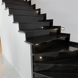 Stonekam - Eleganckie, czarne schody kamienne z subtelnym oświetleniem punktowym w każdym stopniu, kontrastujące z białą ścianą i marmurową podłogą.
