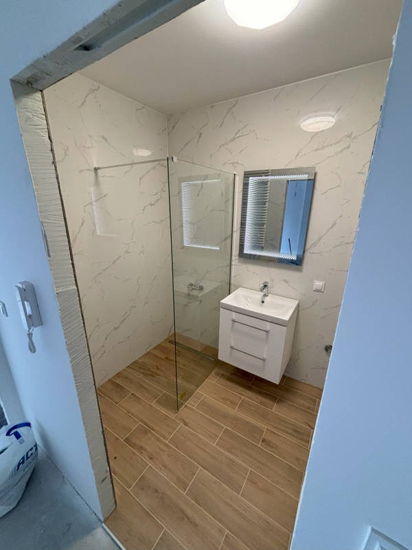 Nowoczesna łazienka po remoncie: kabina prysznicowa ze szklaną ścianką, umywalka z szafką, lustro z podświetleniem i płytki imitujące marmur na ścianach.