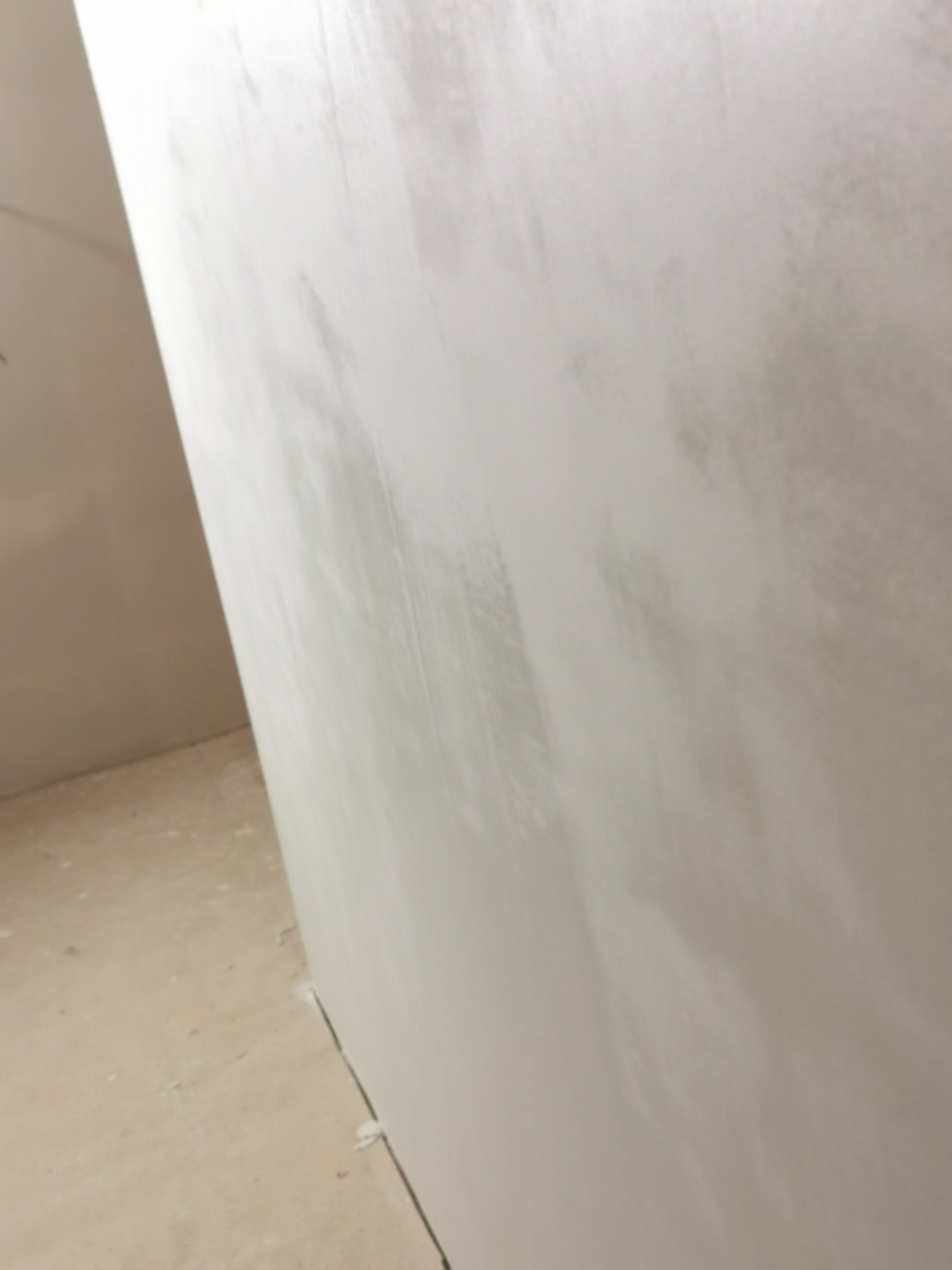 Ściana po nałożeniu gładzi szpachlowej, widoczne delikatne smugi i faktura. Przy podłodze widoczne łączenie ściany z podłożem. Ujęcie z dołu, podkreślające pionowość ściany.