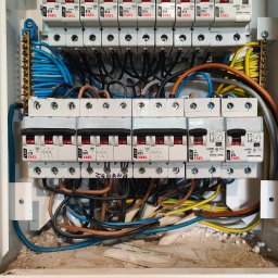 Rozdzielnica elektryczna z bezpiecznikami FAEL, widoczne przewody w różnych kolorach. Instalacja wewnątrz obudowy, z elementami montażowymi i oznaczeniami.