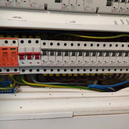 Rozdzielnica elektryczna z zabezpieczeniami przepięciowymi VCX, bezpiecznikami ETIMAT i okablowaniem. Widoczne oznaczenia obwodów: fotowoltaika, pompa ciepła, siła kuchnia.