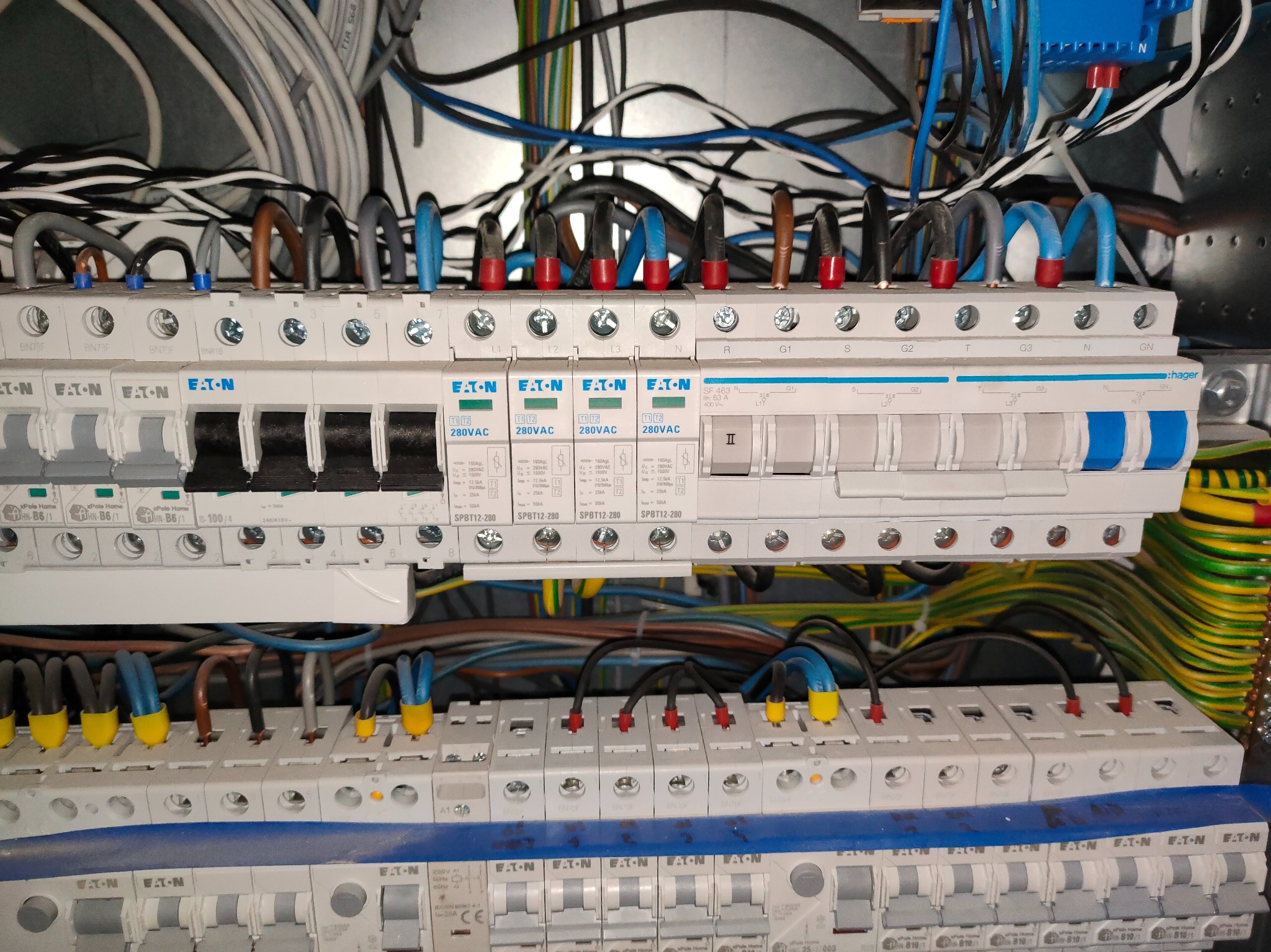 Rozdzielnica elektryczna z widocznymi bezpiecznikami, przewodami w różnych kolorach i oznaczeniami. Widok z bliska na instalację elektryczną wewnątrz skrzynki.