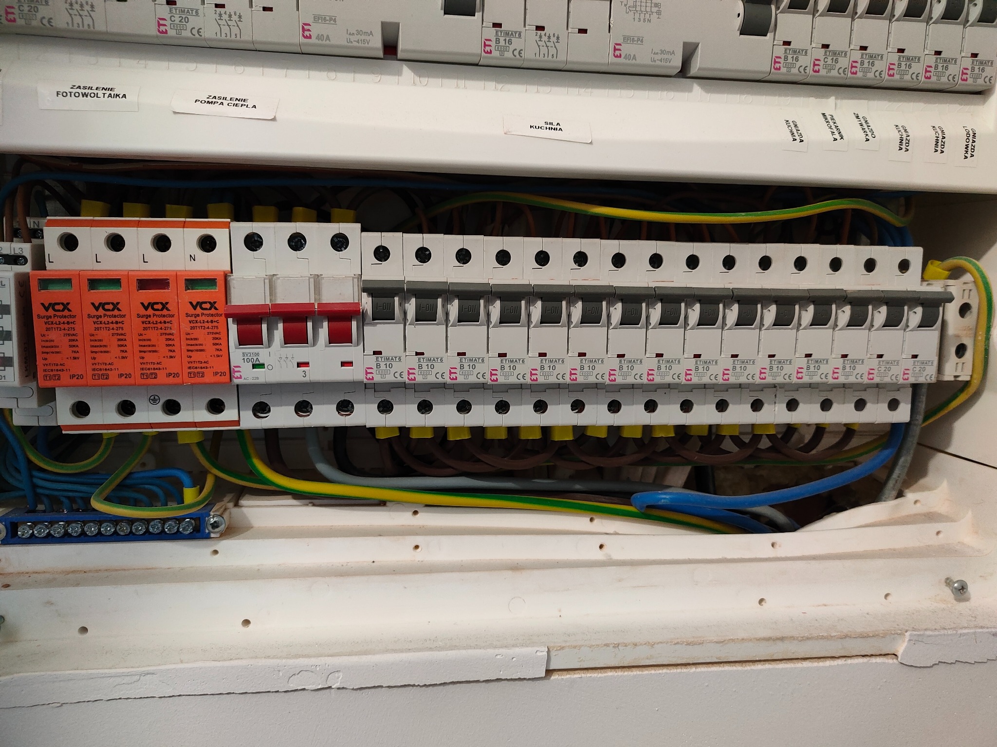 Rozdzielnica elektryczna z zabezpieczeniami przepięciowymi VCX, bezpiecznikami ETIMAT i okablowaniem. Widoczne oznaczenia obwodów: fotowoltaika, pompa ciepła, siła kuchnia.