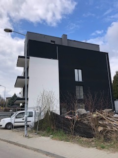 Nowoczesny budynek po renowacji elewacji: czarna ściana kontrastuje z białą, minimalistyczną wstawką. Widoczne balkony i otoczenie miejskie.