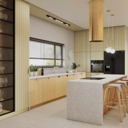 Paula Sch - Jasna kuchnia z drewnianymi szafkami, wyspą z blatem w terrazzo i złotym okapem. Widoczna przeszklona witryna z zastawą i krzesła barowe.