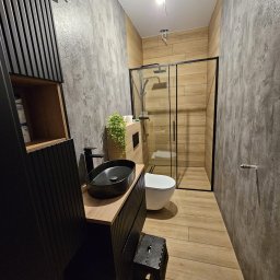 PROJEKT A-Z USŁUGI WYKOŃCZENIOWE - Nowoczesna łazienka z kabiną prysznicową typu walk-in, umywalką nablatową i drewnopodobnymi płytkami. Ściany wykończone w szarym betonie architektonicznym.