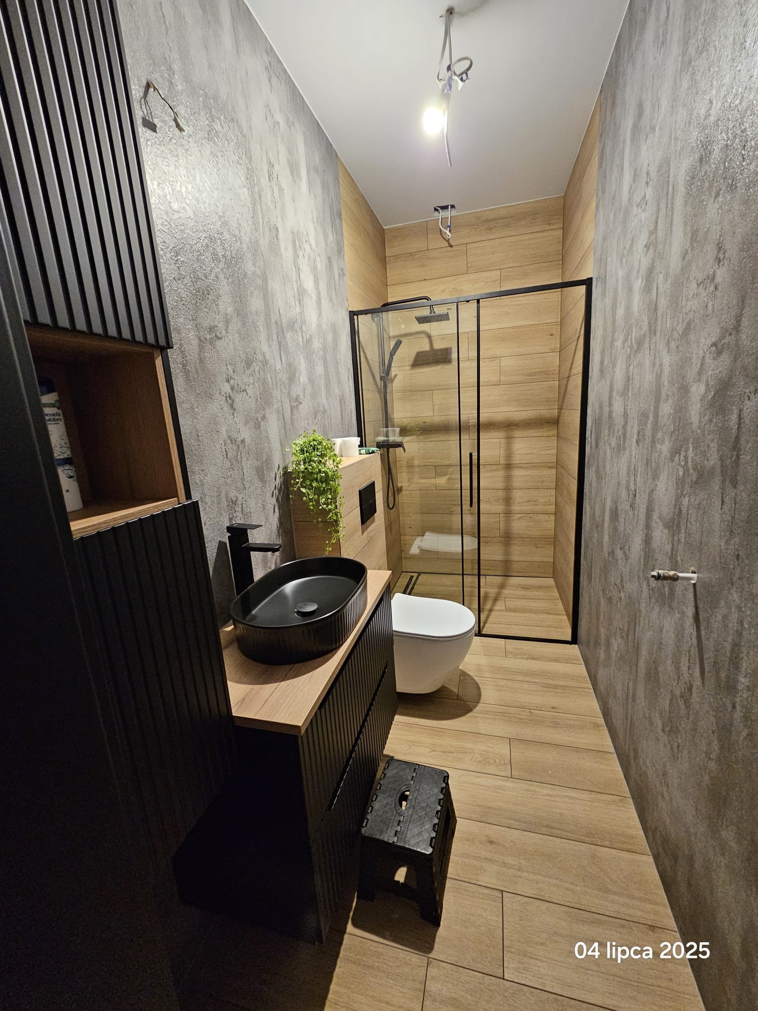 Nowoczesna łazienka z kabiną prysznicową typu walk-in, umywalką nablatową i drewnopodobnymi płytkami. Ściany wykończone w szarym betonie architektonicznym.