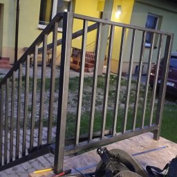 METALWORK KAMIL ŻMUDA USŁUGI SPAWALNICZE - Metalowa konstrukcja schodowa w trakcie montażu przed domem z żółtą elewacją. Widoczne narzędzia i samochód w tle. Ujęcie z dołu.