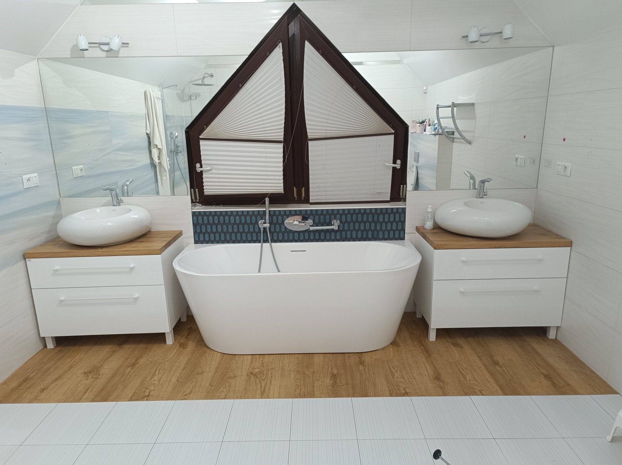 Nowoczesna łazienka w Warszawie: biała wanna wolnostojąca, umywalki nablatowe na drewnianych blatach, lustro i okno w kształcie domku, drewnopodobna podłoga.