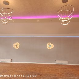 Firma ogólnpobudowlana Dziadkowiec - Jasne wnętrze z parkietem w jodełkę, oświetleniem LED na suficie i ścianach. Dwa nowoczesne, okrągłe żyrandole i dekoracyjne lampy ścienne w kształcie kwiatów.