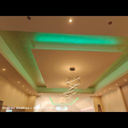 Dziadkowiec usługi ogólnobudowlane - Sufit z podwieszanymi elementami i oświetleniem LED w odcieniach zieleni, nowoczesny żyrandol. Widok z dołu, szeroki kadr.