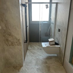 Fachowiec Group SP z o o - Wykończona łazienka z kabiną prysznicową typu walk-in, wiszącą toaletą i marmurowymi płytkami. Widoczne elementy montażowe i pudełko po produkcie.