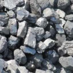 Góra brył węgla drzewnego o nieregularnych kształtach, z widocznymi refleksami światła na powierzchni, przeznaczona do grillowania. Pochodzenie: Ukraina.