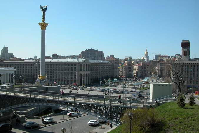 Panorama Kijowa z widokiem na Majdan Nezaleznosti (Plac Niepodległości) z pomnikiem Archanioła Michała na kolumnie, mostem dla pieszych i budynkami w tle.