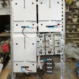 MICHAŁ Z NAPIĘCIEM MICHAŁ PAWLAK - Rozdzielnica elektryczna w metalowej obudowie z zamontowanymi bezpiecznikami Eaton, przewodami i listwami zaciskowymi. Widoczne narzędzia i elementy instalacji.