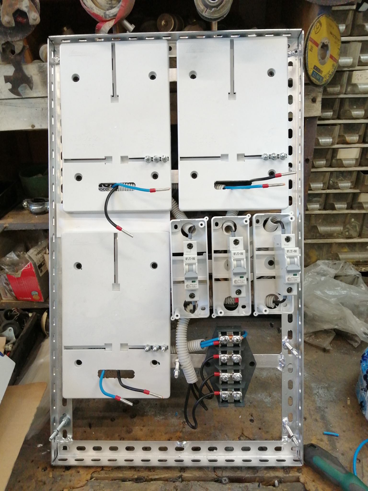 Rozdzielnica elektryczna w metalowej obudowie z zamontowanymi bezpiecznikami Eaton, przewodami i listwami zaciskowymi. Widoczne narzędzia i elementy instalacji.