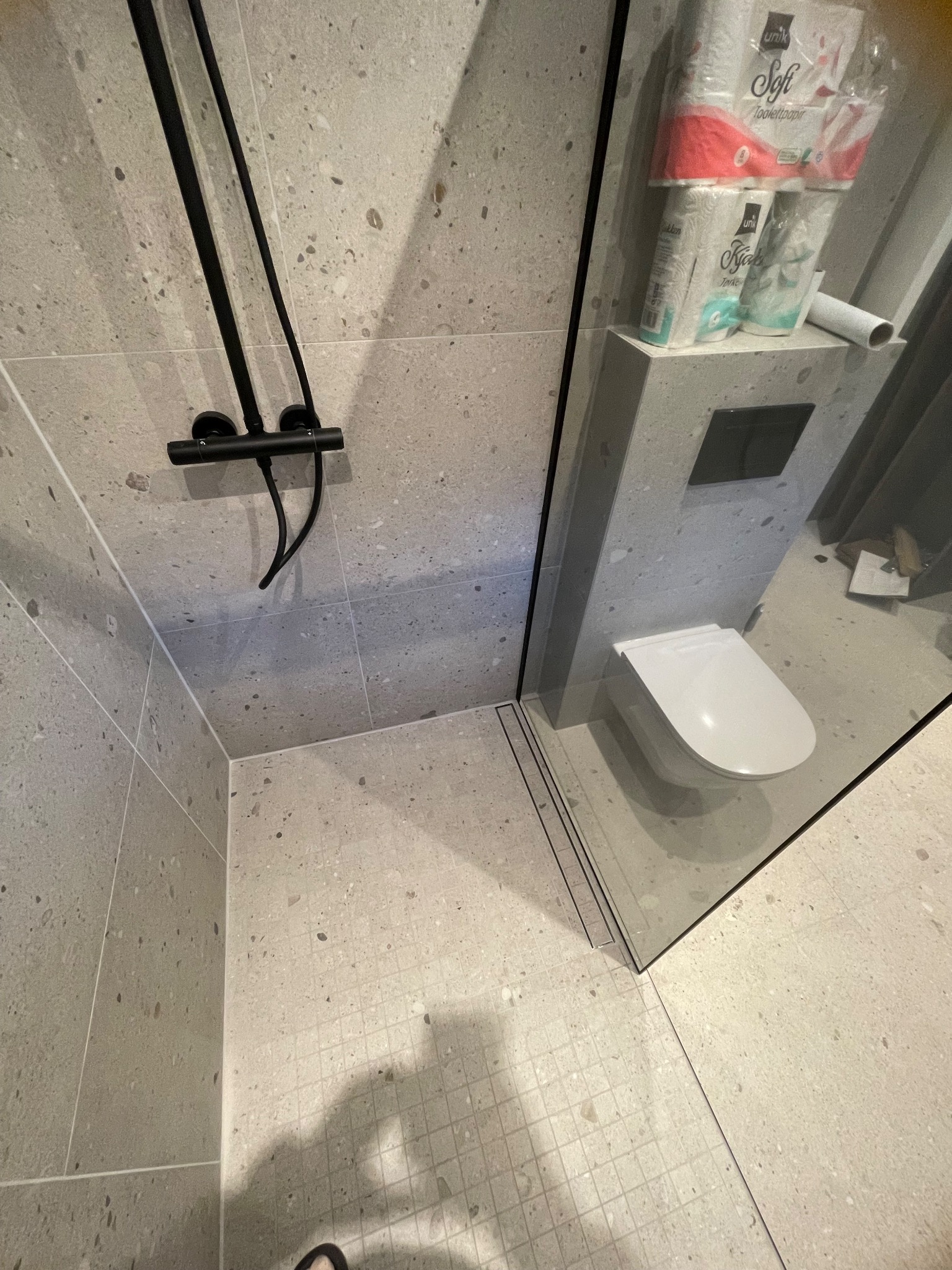 Wykończona łazienka z kabiną typu walk-in, szarą terakotą, czarną armaturą i podwieszaną toaletą. Widok z góry, podkreślający minimalistyczny design.